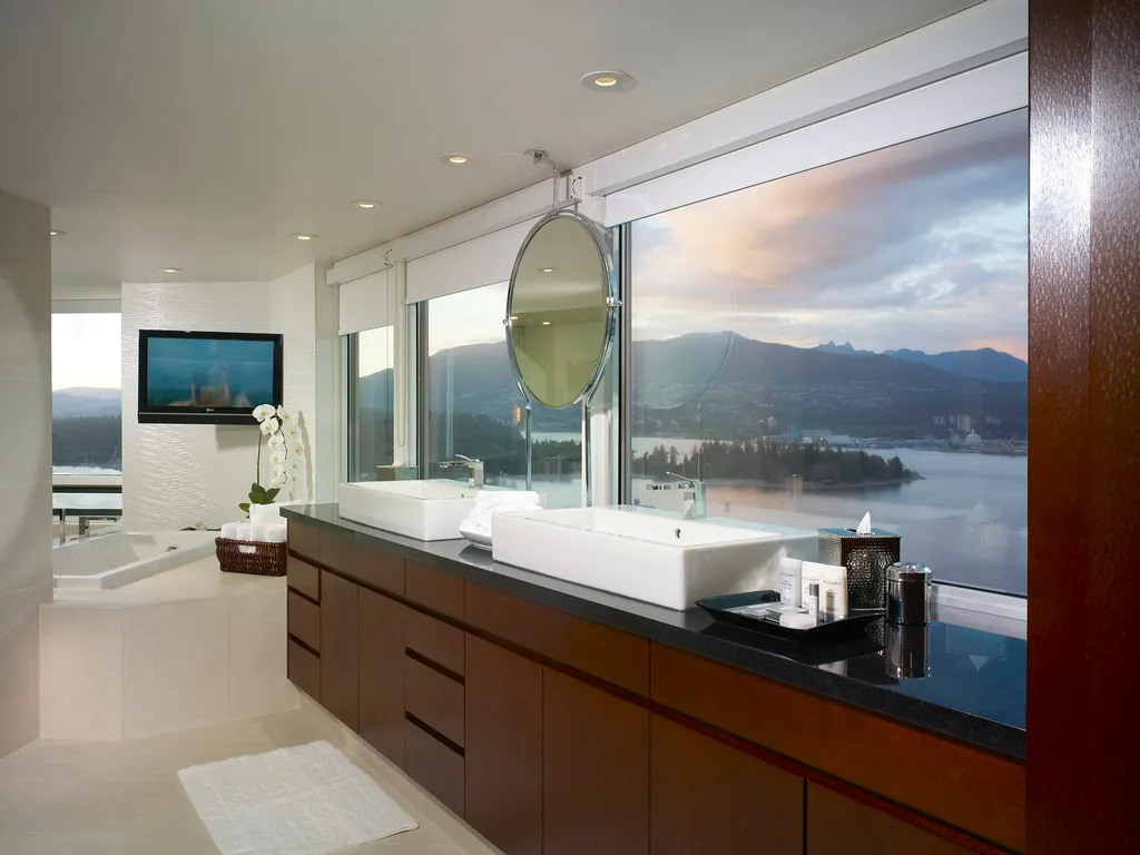 Editorial luxury bathroom with stone-topped vanity and tiled tub surround overlooking a harbor