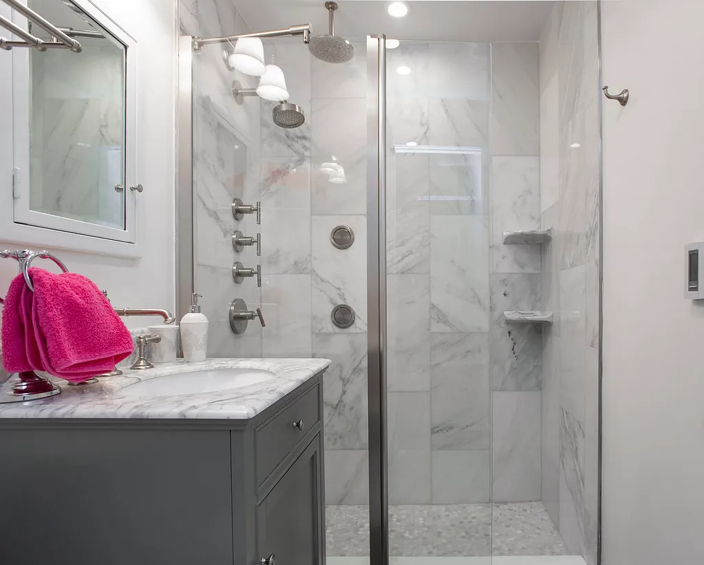 Marble-tiled walk-in shower with niche shelves next to a gray vanity