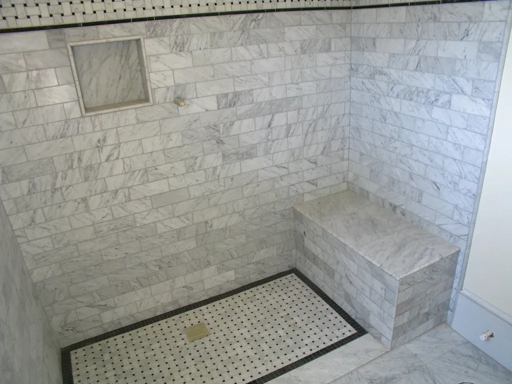 Marble-tiled walk-in shower with a bench seat and mosaic tile floor