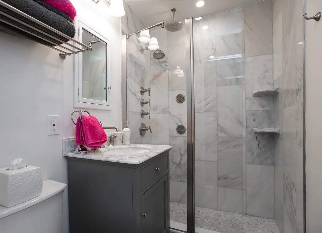 Gray marble-tiled walk-in shower beside a vanity with marble countertop
